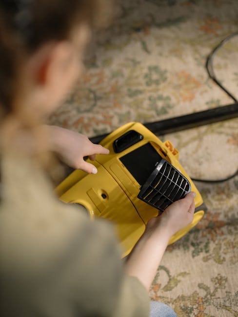 A black and red vacuum cleaner with a transparent dust container and foamy residue inside, positioned on a pink textured carpet in a residential room. The vacuum's flexible, patterned hose is connecte