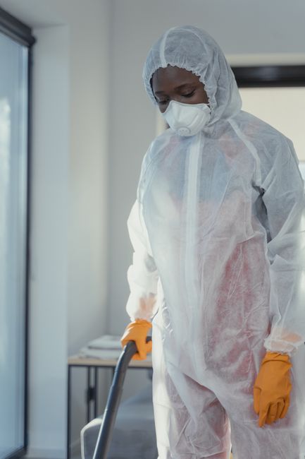 A person kneeling on a patterned rug in a room, emptying a yellow and black vacuum cleaner with a clear dust container. The room features wooden flooring, visible in the background, and is well-lit, h