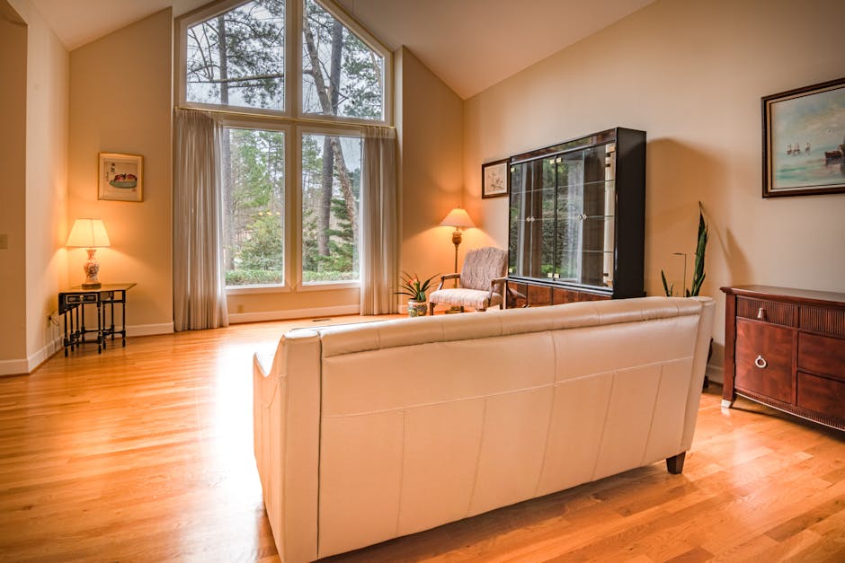 A white upholstered sofa in a room with white paneled walls and wooden flooring. The sofa features rolled arms with tufted detailing and dark wooden legs. The space is well-lit, highlighting the clean